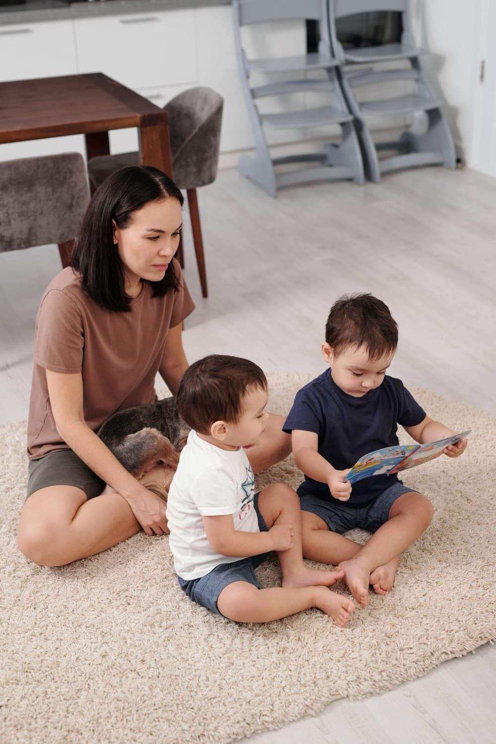 A woman reading a picture book with two toddlers on the living room rug