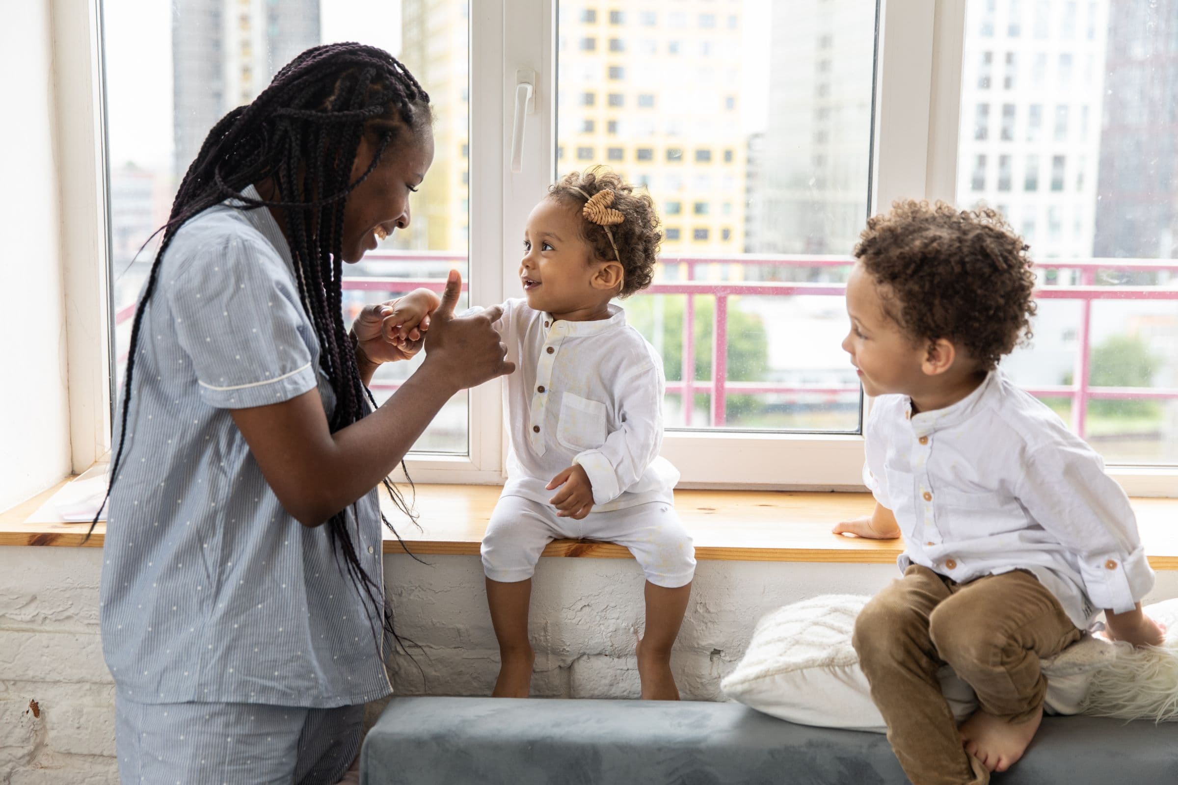 A nanny playing with two toddlers by a sunny window